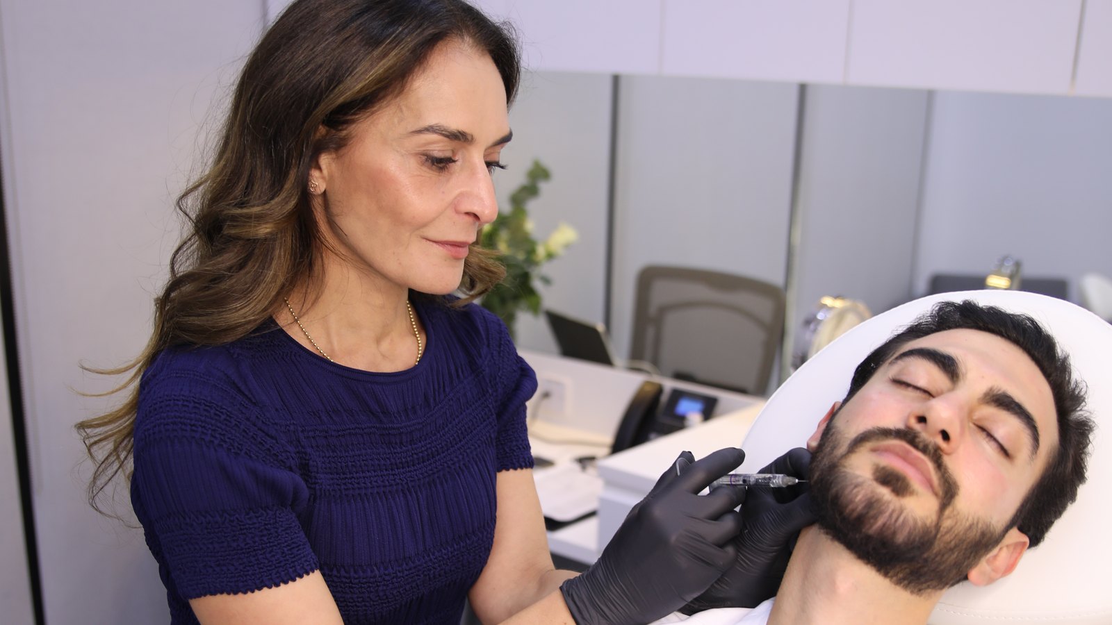 Dr Suha Kersh of 23MD giving a dermal filler injection along a male patient's jawline at the 23MD Dubai clinic